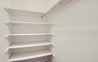 a walk in closet with white shelving and a wood floor