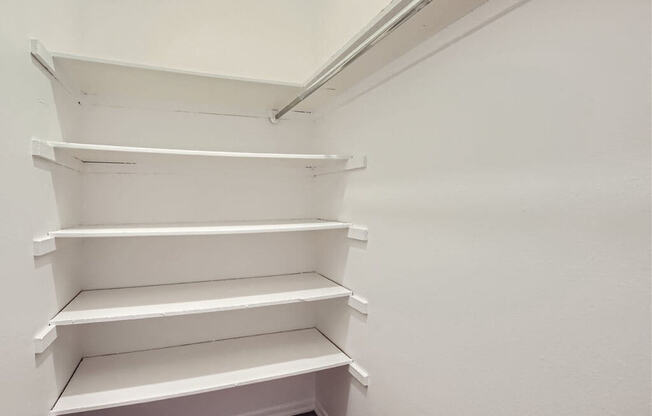 a walk in closet with white shelving and a wood floor