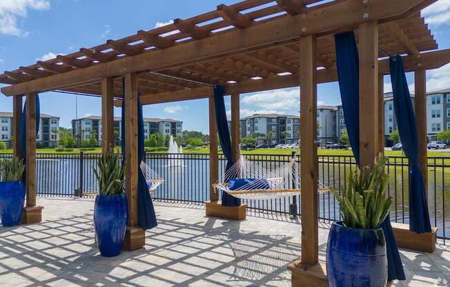A wooden pergola with blue vases and plants is in the foreground with apartment buildings in the background.
