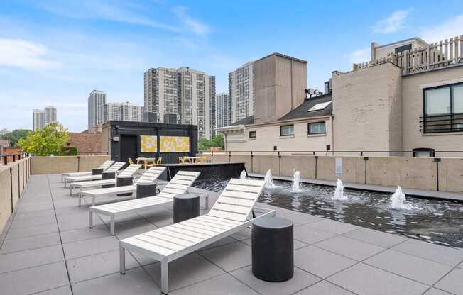 the rooftop pool of a building with white lounge chairs and a fountain