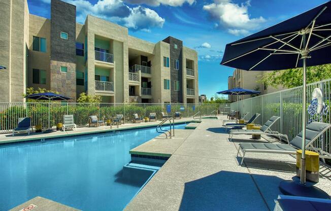 The Craft at Gilbert and Baseline Pool with buildings in the background and patio umbrella up front. Four lounge chairs line the pool.