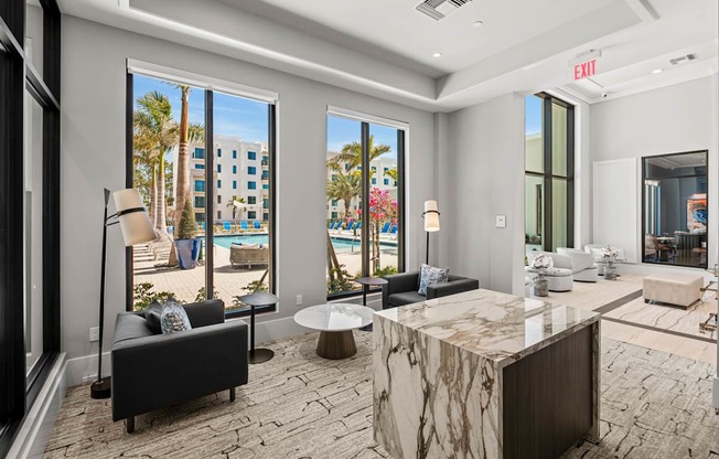 A modern living room with a marble table and a view of a pool and palm trees.