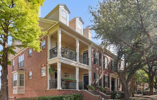 A red brick house with a balcony and a tree in front.