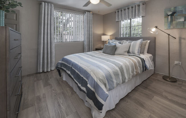 Bedroom with two large windows, fan, wood-style floor, and model furnishings at Terraces at Clearwater Beach, Florida