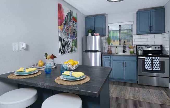 Fusion Las Vegas apartment kitchen with blue cabinets with black pulls, electric stove, and stainless steel refrigerator.