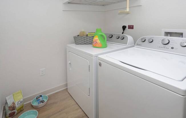 A laundry room with a washer and dryer and a basket of detergent.