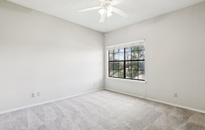 Second bedroom of B1 floor plan with large window and ceiling fan at Jefferson Creek Apartments in Irving, TX.