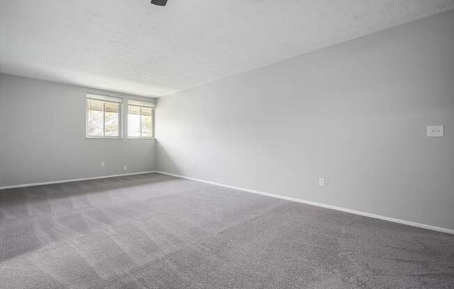 an empty room with a carpeted floor and two windows