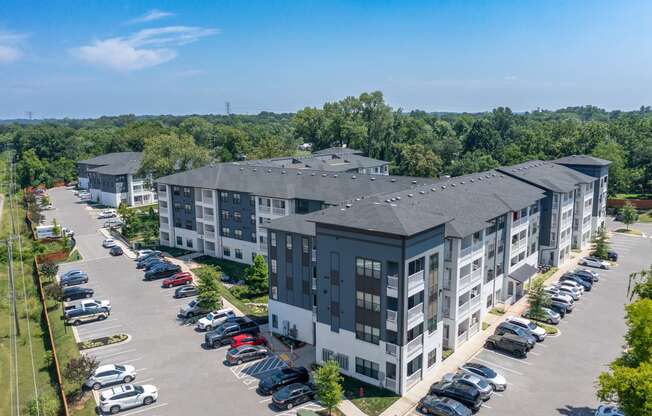 an aerial view of a large apartment complex with a parking lot and trees in the background