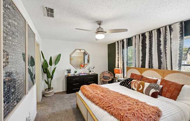 A bedroom with a bed, dresser, mirror, and a plant.