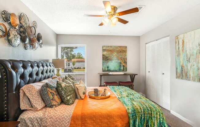 A bedroom with a black headboard and a bed with orange and green bedspread.