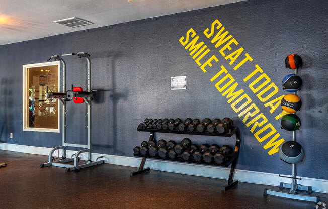 a fitness room with weights and a wall with a sign that says sweat the gym at Water Ridge, Texas