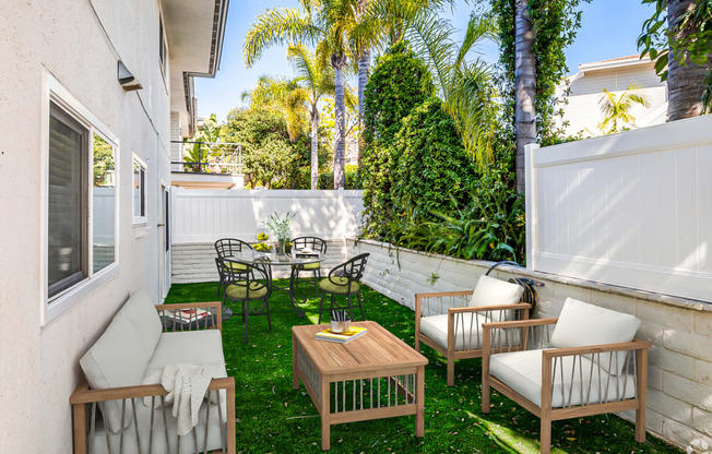 a patio with a wooden table and chairs and a white fence