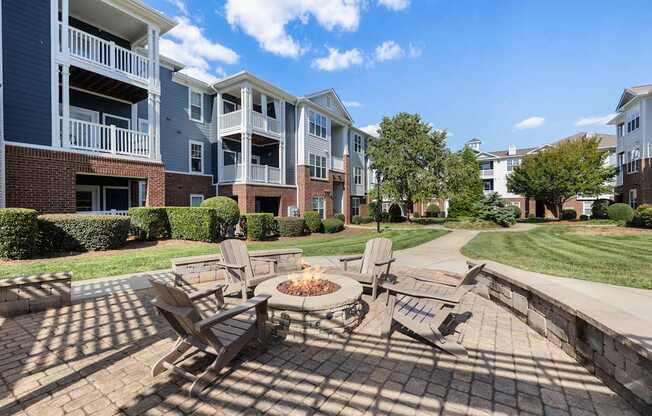 A patio with chairs and a fire pit in front of apartment buildings.