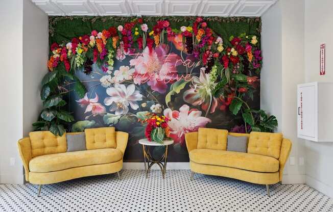 Two yellow couches in front of a floral mural.