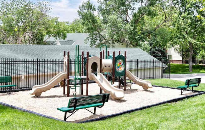 A playground with a green slide, a sandbox, and a wooden structure.