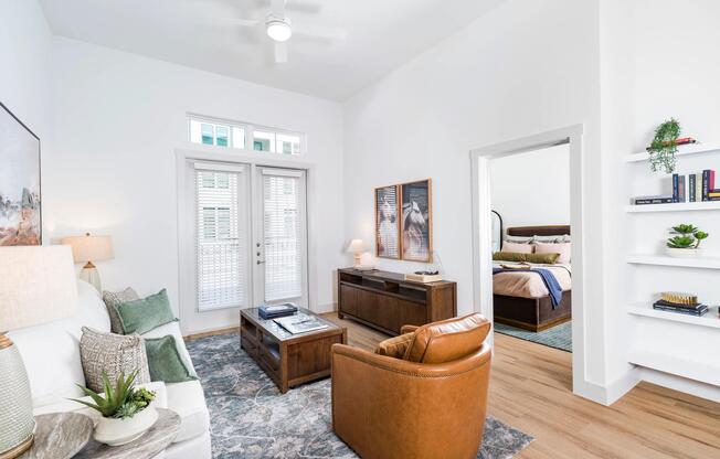 Open living area with high ceilings, built-in shelving, and French doors that bring in daylight and connect the living space to the outdoors.