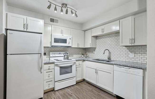 A white kitchen with a refrigerator, microwave, oven, and sink.