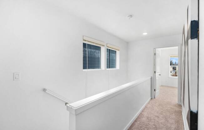a hallway with white walls and two windows and a white staircase