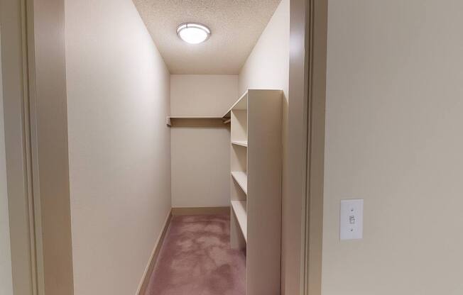 A spacious walk-in closet here at Whispering Cedars with soft carpet, built-in shelving, and a hanging rod, offering ample storage space and an organized layout for comfortable, convenient living.