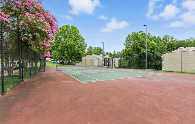 A tennis court surrounded by green trees and buildings.