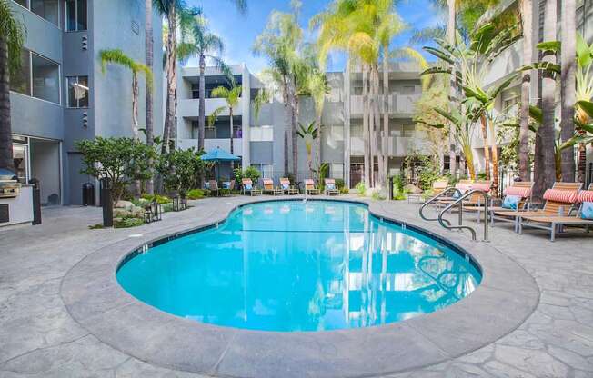 A round swimming pool surrounded by palm trees and lounge chairs.