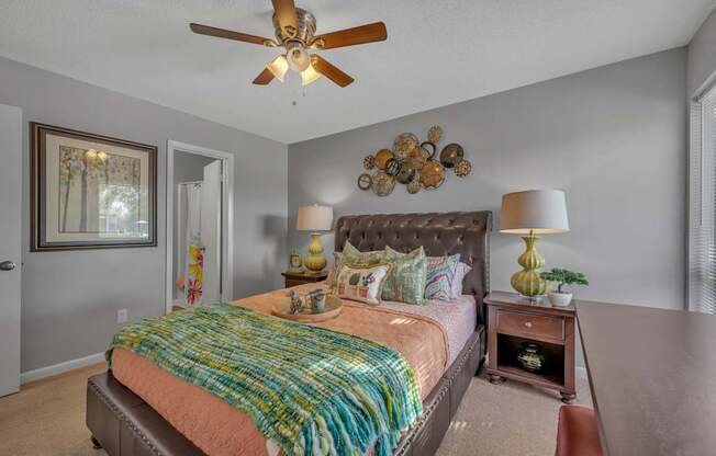 A bedroom with a bed, a ceiling fan, and a wall decoration.