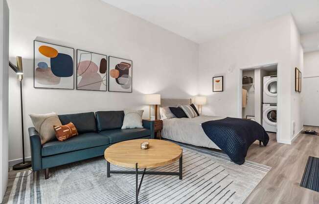 A modern living room with a blue couch, a coffee table, and a bed with a blue blanket.
