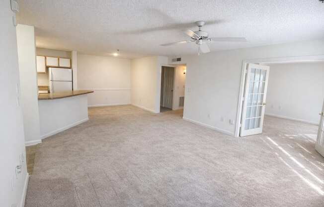 A spacious living room with a ceiling fan and carpeted floor.