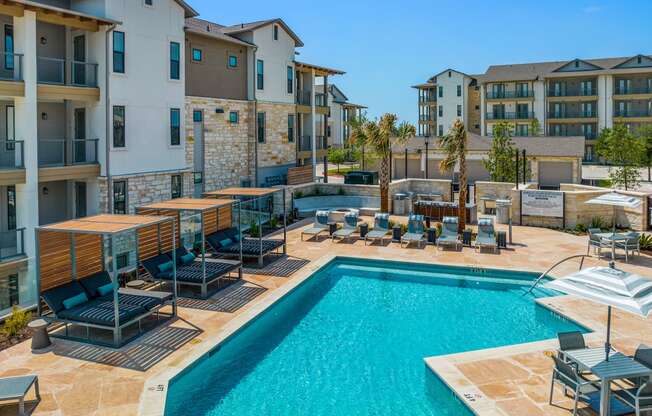 a swimming pool with chairs and umbrellas in front of an apartment building