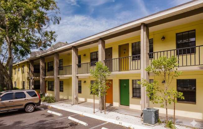 A yellow building with a green door and a tree in front of it.