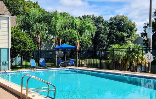 a swimming pool with a blue umbrella and chairs