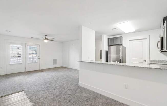 A spacious room with a ceiling fan and a kitchenette in the background.