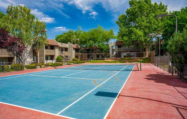 A tennis court with a red and blue surface surrounded by apartment buildings.
