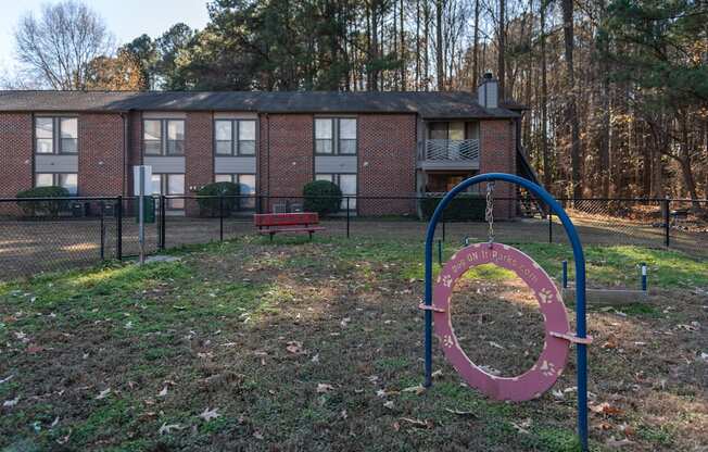 A playground with a red and blue swing set in front of a brick building.