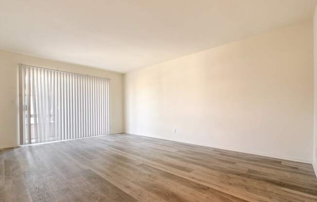 Living room with wood-inspired floors, balcony on the left with vertical blinds