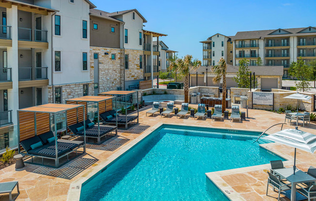 a swimming pool with chairs and umbrellas in front of an apartment building
