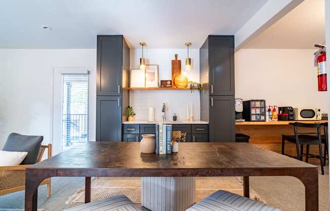a living room with a wooden table and a kitchen with grey cabinets