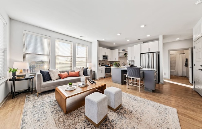 A modern living room with a grey sofa, a wooden coffee table, and a kitchen area in the background