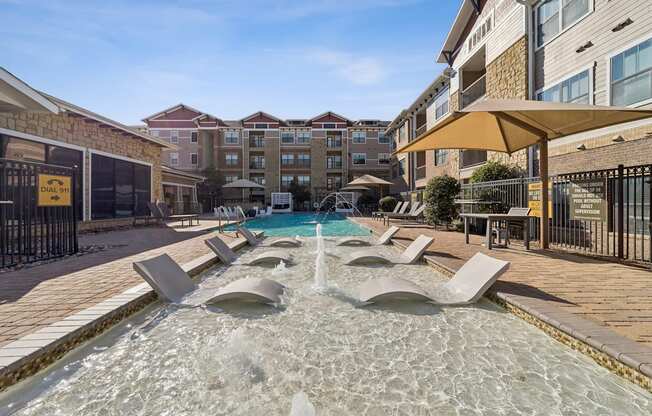 A fountain in the middle of a pool surrounded by lounge chairs.