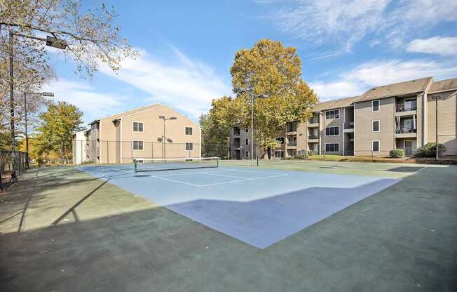 A tennis court is surrounded by apartment buildings.