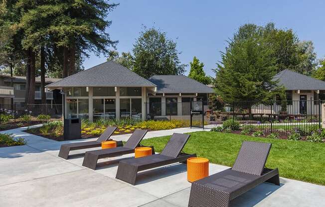 Concrete pool deck with brown deck chairs and orange tables. Grass, club house and lounge behind them.