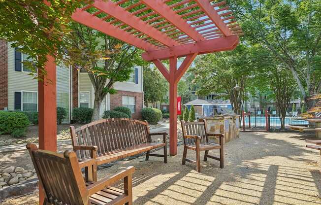 A wooden bench under a red pergola in a sunny park.
