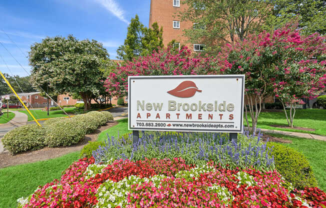 A sign for New Brookside Apartments is surrounded by flowers.