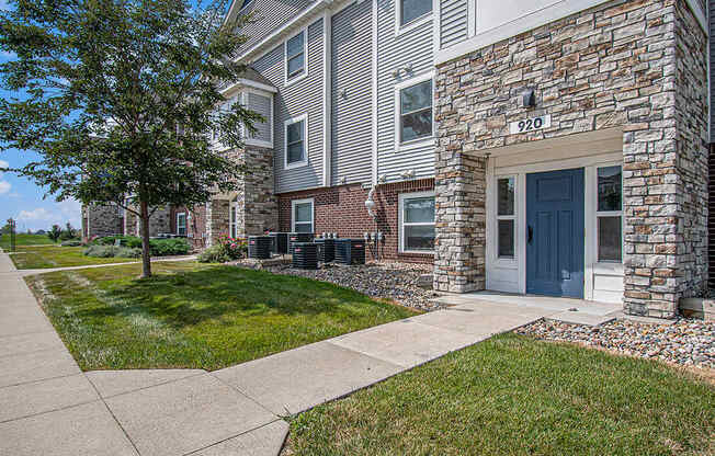 An apartment building with stone and a tree in front at The Reserve at Destination Pointe, Grimes, Iowa