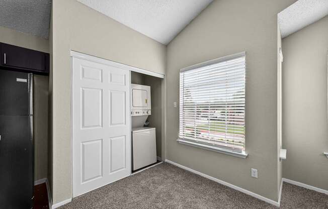 A room with a white door, a window with blinds, and a black refrigerator.
