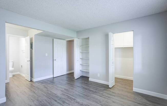 A room with white walls and wood flooring with a doorway leading to another room.