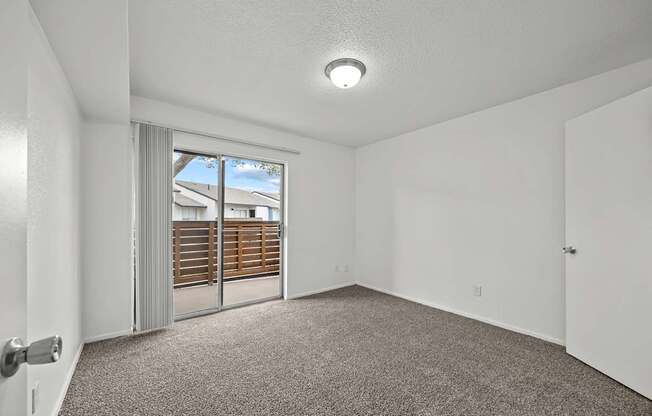 A room with a carpeted floor and a sliding glass door leading to a balcony.