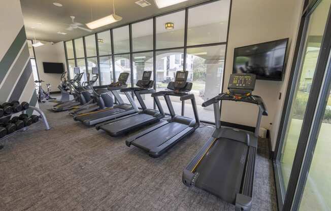 a gym with cardio machines and a tv
