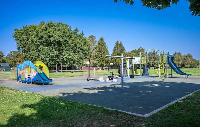 A playground with a yellow and blue slide, a green swing set, and a red and white seesaw.